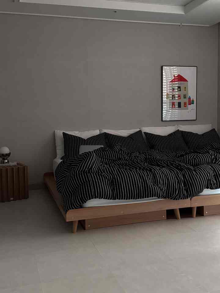 ナチュラルカラーでモダンな寝室、木製ベッドフレームと黒のストライプ柄寝具が配置された落ち着いた雰囲気のインテリア