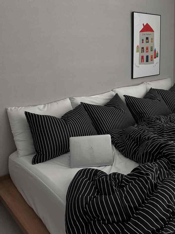 White bedroom with black striped bedding, featuring a MacBook on bed creating a modern and clean atmosphere