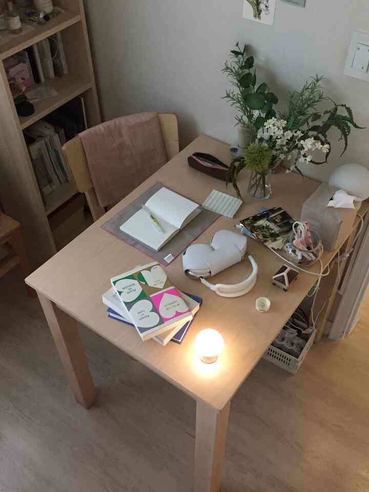 ナチュラルな木目調のホームオフィス、木製テーブルと本棚、花瓶やノートが配置された雰囲気のある作業空間