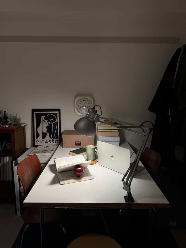 White-walled Mid-Century Modern home office featuring a white desk, wooden chairs, books, and a desk lamp with cozy ambiance