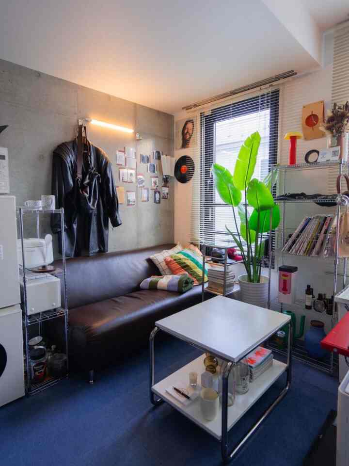 黒いレザーソファと大きな緑色のフェイクプラントがあるワンルーム、コンパクトで整ったレイアウトの空間