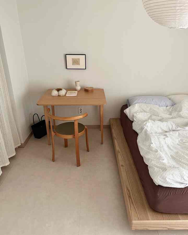 ベージュ色の床と木製ベッドフレーム、シンプルな机と椅子が配置された落ち着いた寝室のインテリア