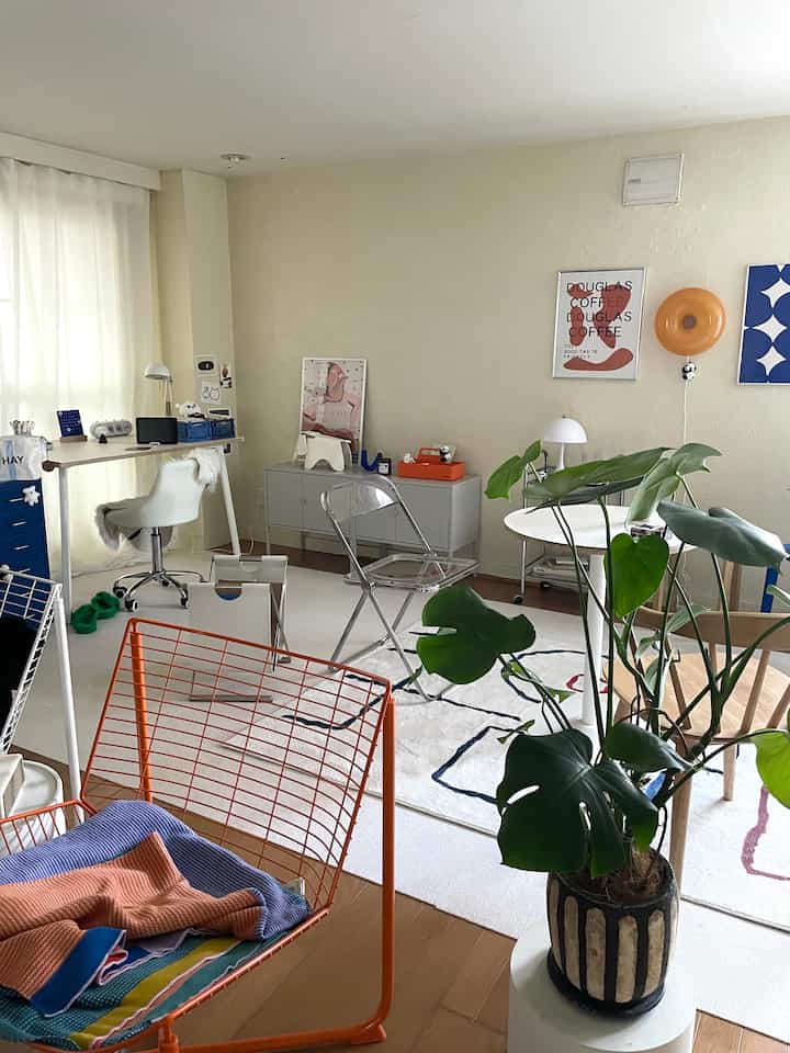 白とオレンジの調和がある二人暮らし向けのリビング兼ワークスペース、ダイニングチェアとデスク、大きな観葉植物が配置された雰囲気のある空間