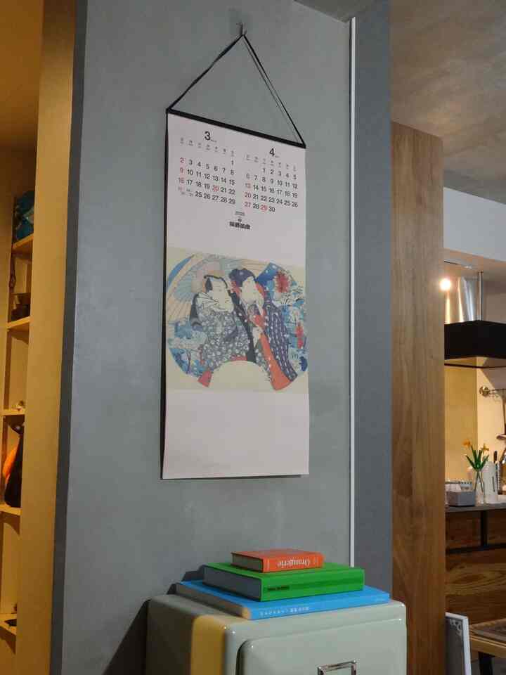 Modern single household kitchen with gray wall featuring a large Japanese wall calendar and a small cabinet topped with books