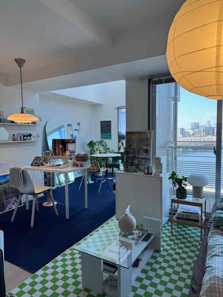 ブルーのカーペットと緑のチェック柄ラグが調和するワンルーム、デスクやソファ、多彩な植物が配置されたミッドセンチュリーモダンの印象的な空間