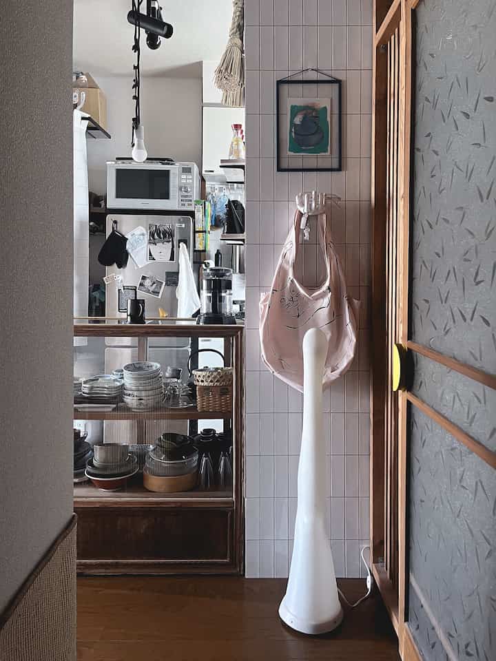 ナチュラルな色調の2DK玄関とキッチンスペース、猫のイラストバッグとアートが配置された落ち着いた一人暮らしの空間