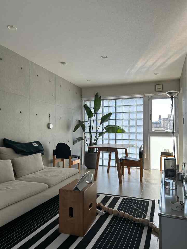 白とグレーのトーンのリビング、ナチュラルな木製家具と大きな植物が配置された雰囲気のあるモダンな空間