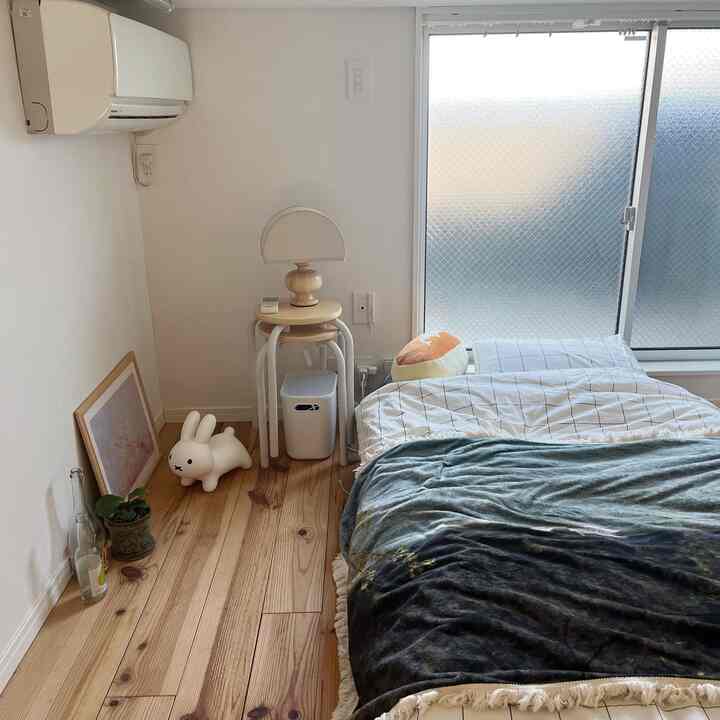 ナチュラルカラーと木目調が調和したワンルームの寝室、左側にスツールとテーブルランプが配置された落ち着いた空間