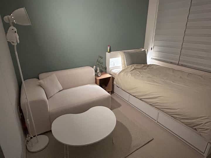 白とベージュのトーンのワンルーム寝室、シンプルでナチュラルな雰囲気のソファとナイトテーブルが配置された空間