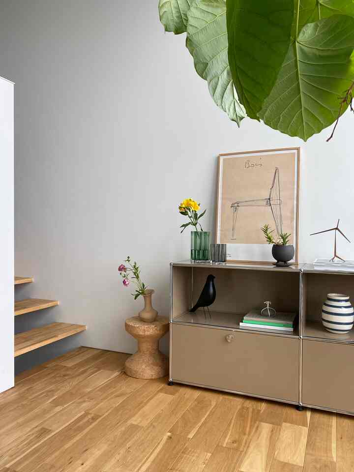 ナチュラルな木目調の床とベージュのサイドボードが配置された玄関またはリビング、植物と花瓶で飾られたシンプルで落ち着いた雰囲気のインテリア