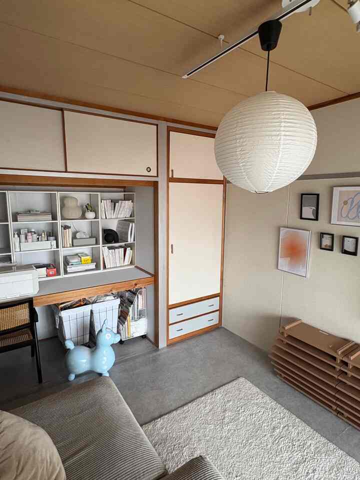 ナチュラルな色調と木目調が特徴のリビングルーム、ベージュのソファと白いラグ、壁にポスターが飾られた落ち着いた空間