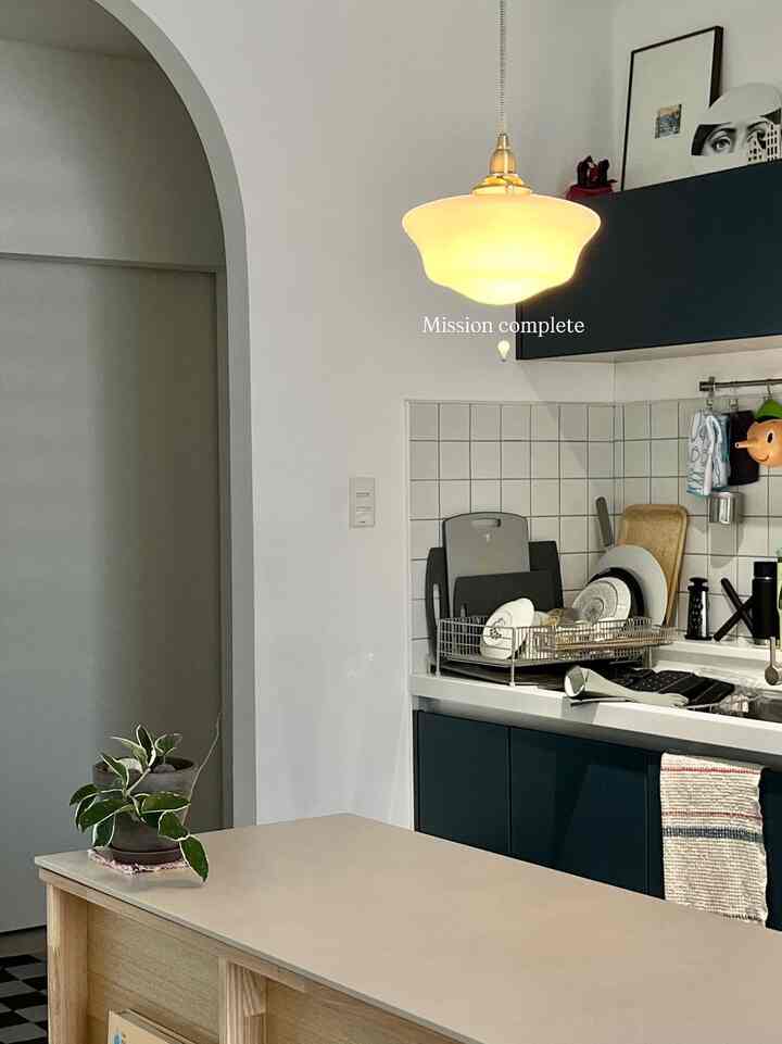Kitchen with white walls and navy lower cabinets, featuring a classic pendant light over the kitchen island creating a cozy and clean atmosphere