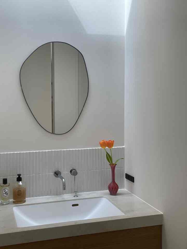 ホワイトとナチュラルカラーのバスルーム、シンプルで印象的な鏡とオレンジのチューリップが配置された空間