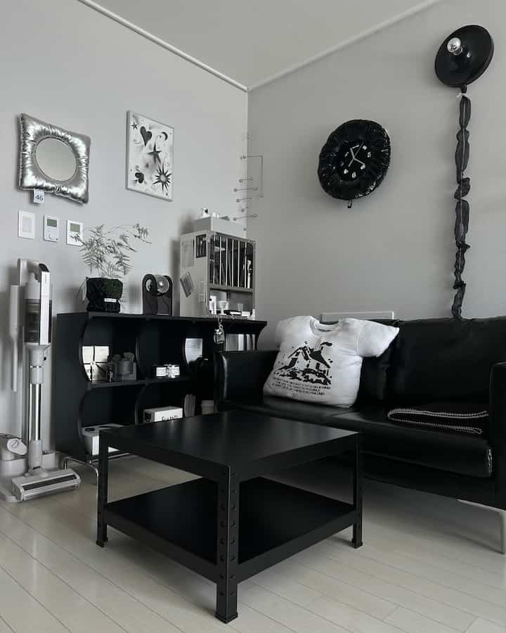 黒とグレーのトーンのワンルームリビング、黒のソファとコーヒーテーブル、壁時計や様々なインテリア小物が配置されたモダンでミニマルな空間