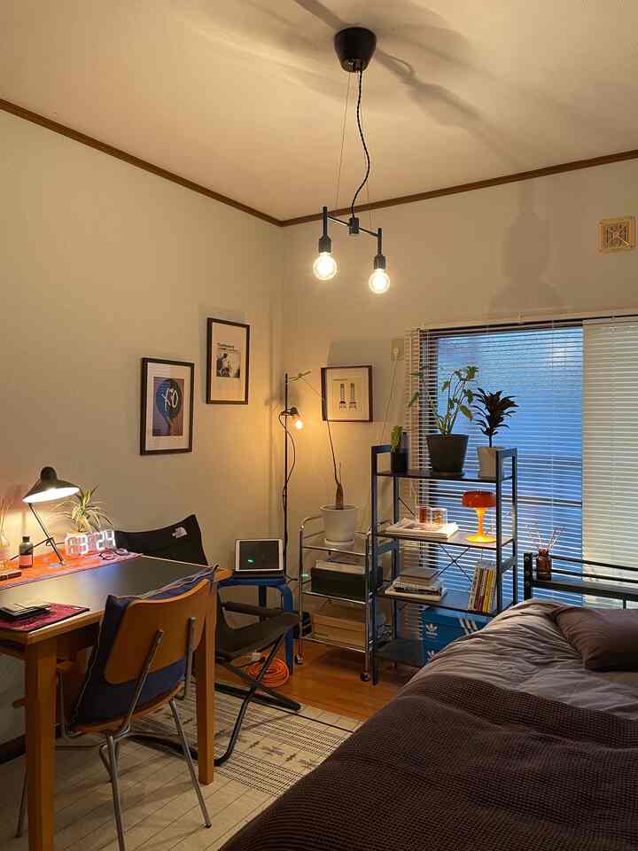 暖かいブラウンとオレンジの色調の一人暮らし寝室、デスクとペンダントライトが配置された雰囲気のある空間