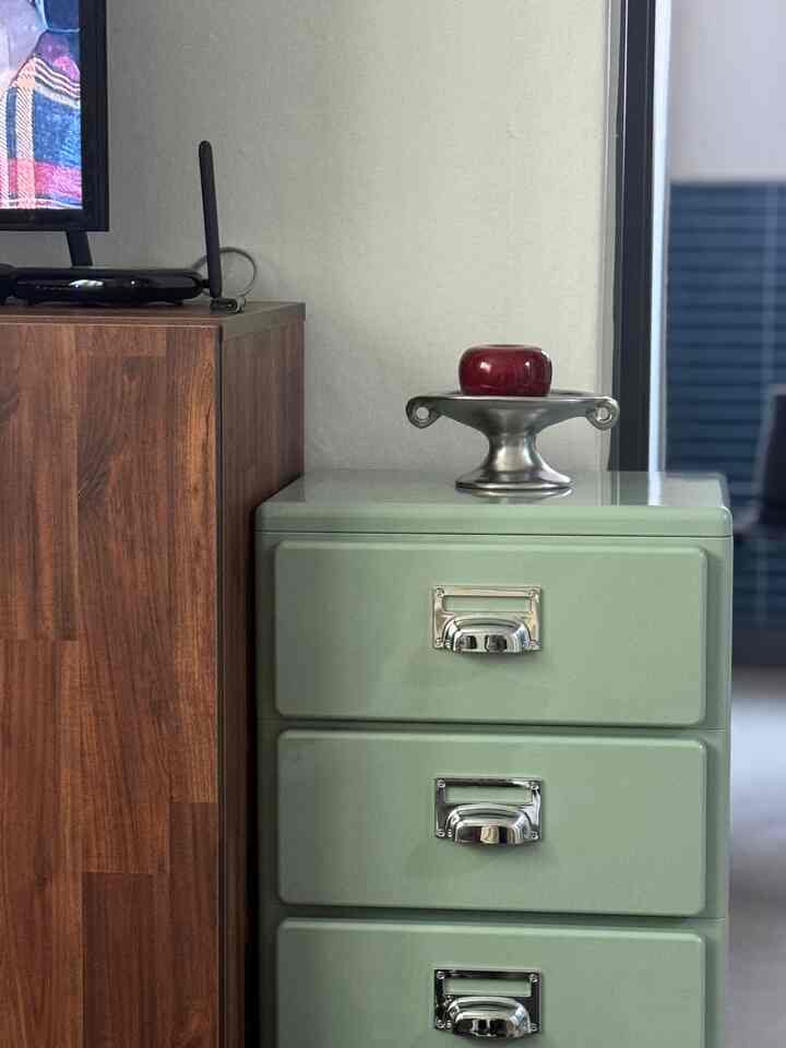 淡いグリーンのドレッサーの上にシルバーのトレイと赤いリンゴのオブジェが置かれたミッドセンチュリーモダンのリビングルーム