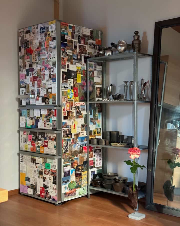 グレーとウッドトーンの床がある1LDKの空間、ステッカーで覆われた冷蔵庫と金属製の棚、花瓶が配置された雰囲気のあるインテリア