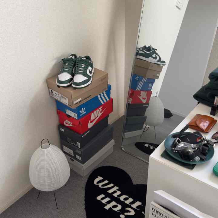 Small corner room with bright white walls and full-length mirror, stacked shoe boxes and floor lamp creating an organized space