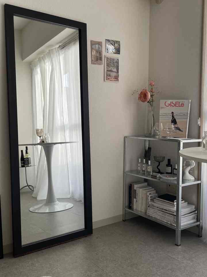 Narrow room with white and silver tones featuring a large black-framed mirror and silver shelving unit in a simple minimal interior
