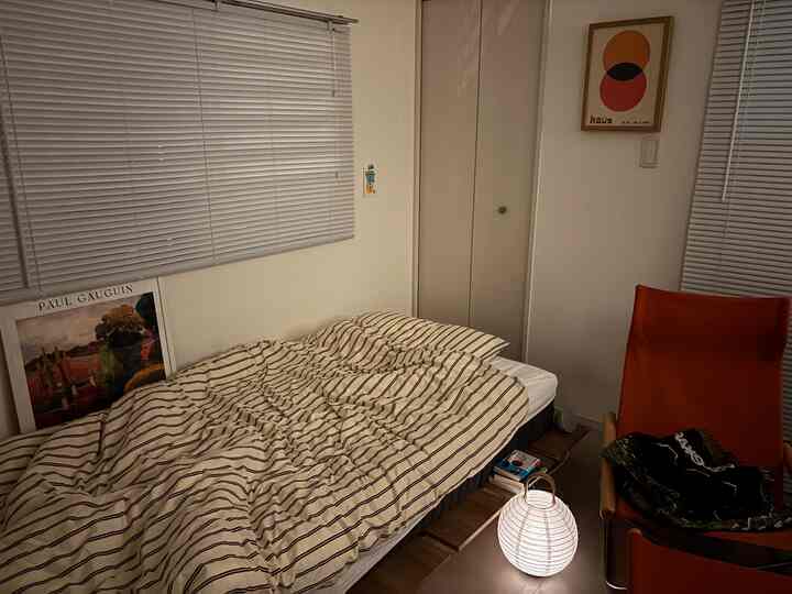 Modern bedroom in white and brown tones featuring a bed with striped duvet cover and an orange armchair