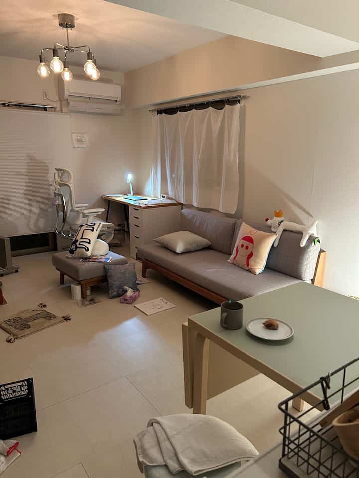 Natural beige-toned living room featuring sofa, ottoman, desk, and green table in a cozy setting