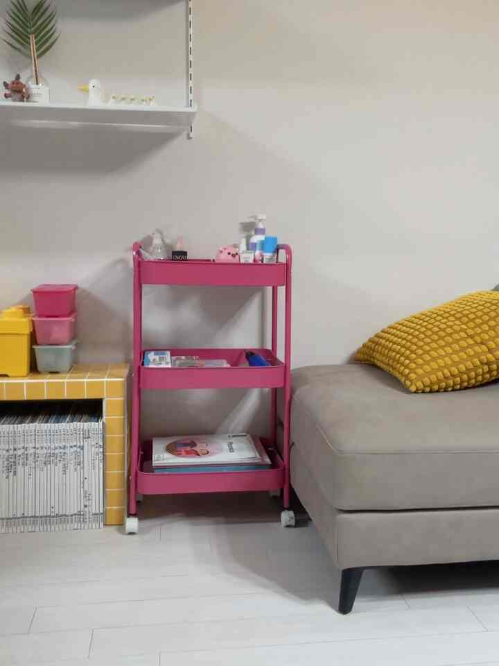 ナチュラルな雰囲気の狭い部屋、ベージュのソファとピンクの移動式トロリーが配置されたインテリア