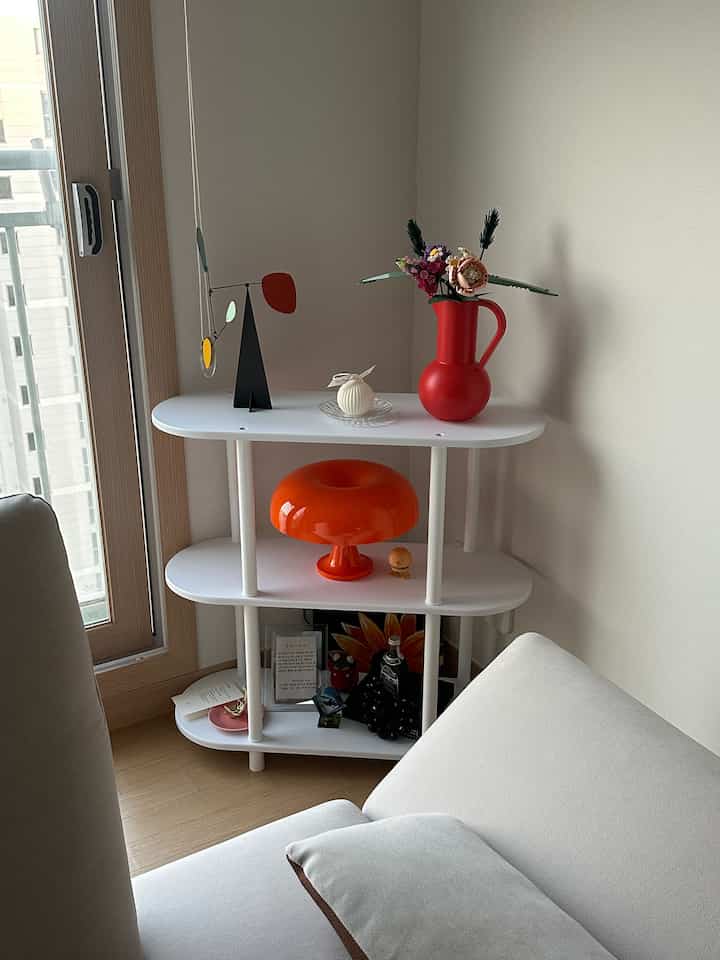 白い壁とナチュラルウッドの床、コーナーに配置された白い棚とベージュのソファがあるミニマルで清潔感のあるリビングルーム