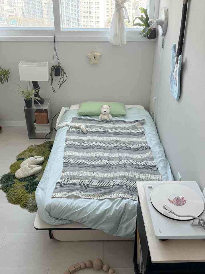 白と淡いブルーのトーンの小さなワンルーム寝室、シンプルな家具と植物が配置された雰囲気のあるインテリア