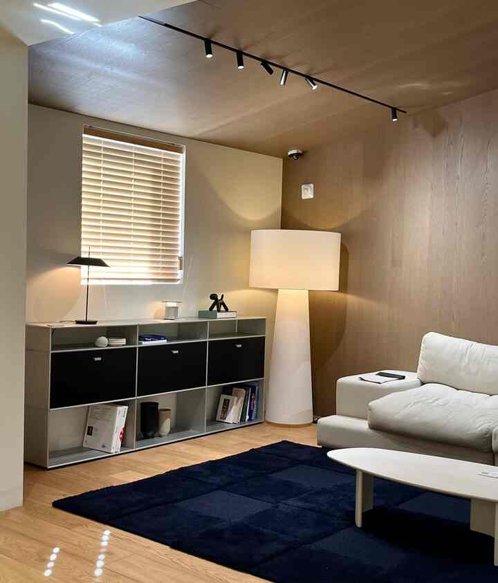 白いソファとネイビーのラグ、木目調の壁、フロアランプが配置されたモダンなリビング