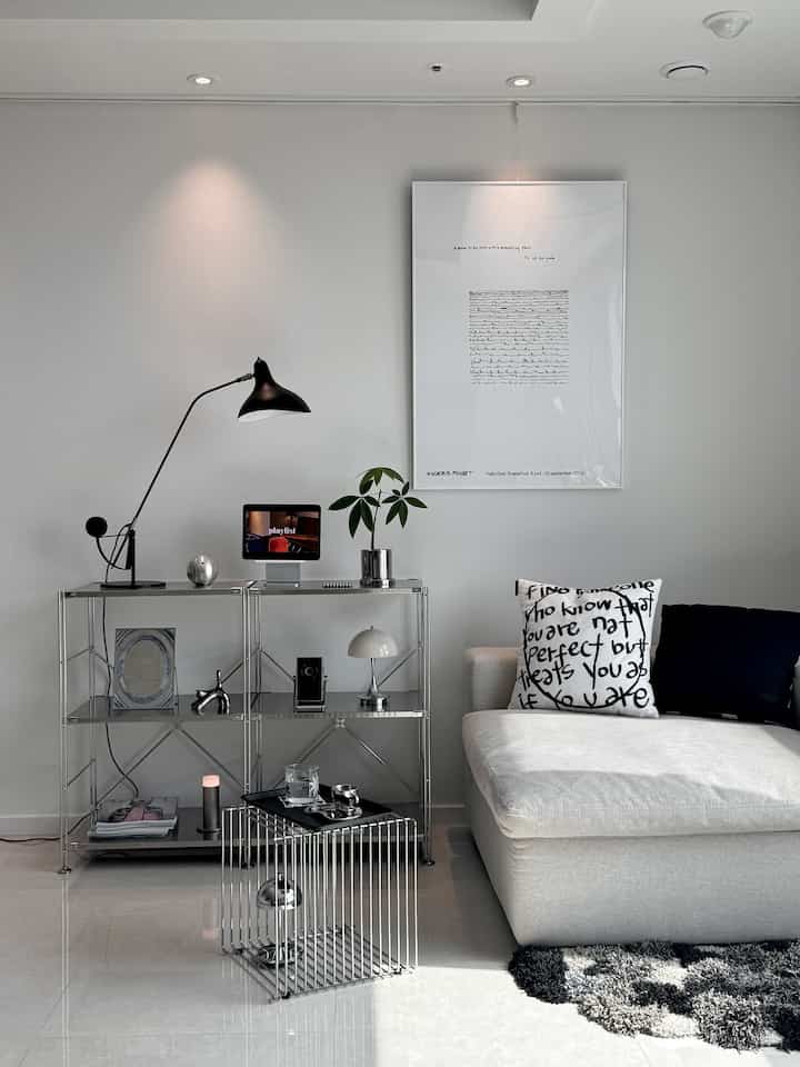 白とシルバーの調和が取れたリビング、ステンレス棚とベージュのソファが配置されたモダンな空間