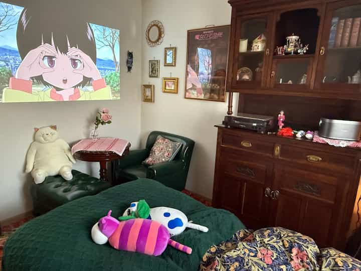 A bedroom with green bedding and antique furniture, featuring an anime projection on the white wall creating a retro atmosphere