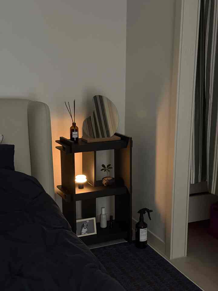 ブラックとホワイトのトーンの寝室、黒のナイトテーブルに点灯したテーブルランプとディフューザーが置かれた清潔な空間