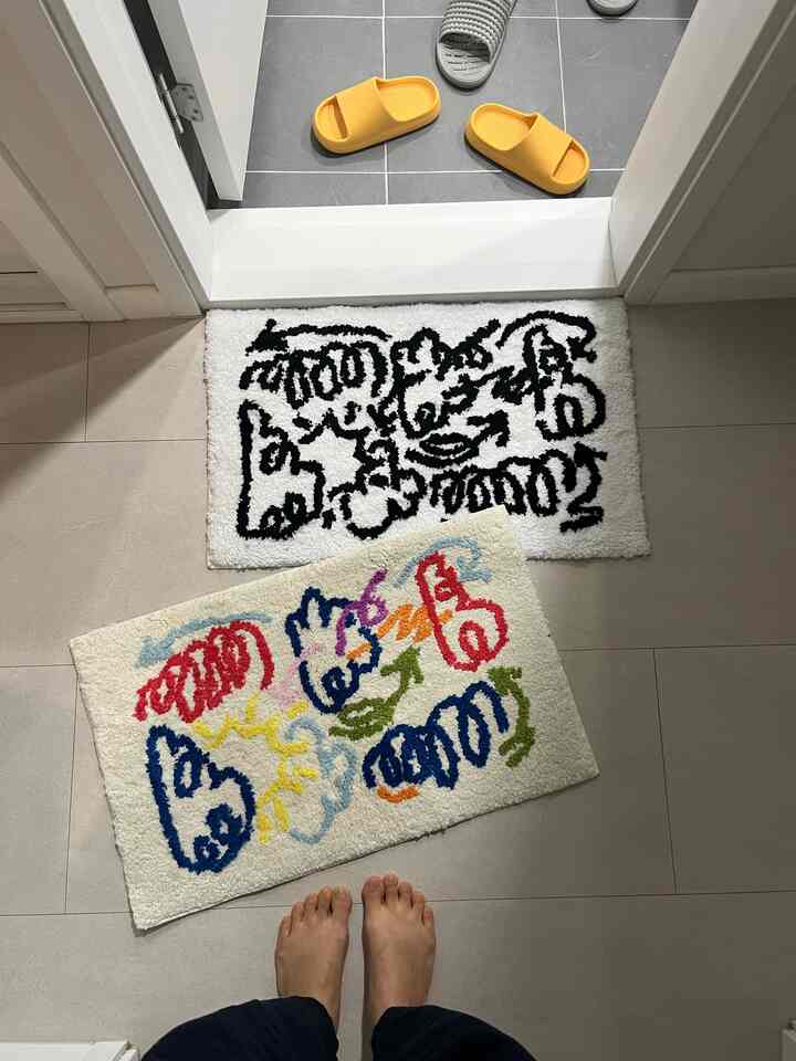 白い床のバスルームに黒とカラフルな落書き柄のミニラグが2枚配置された雰囲気のあるインテリア