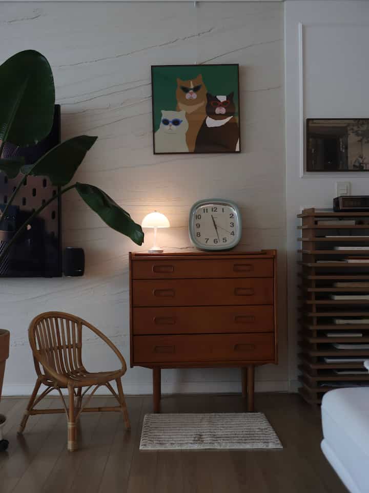 Brown and natural toned living room featuring wooden chest, rattan chair, small rug, and a framed cat illustration creating a cozy atmosphere