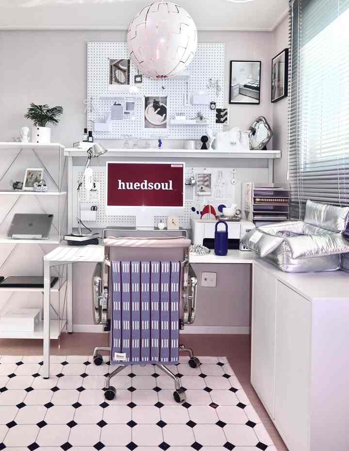 モノトーンでモダンなホームオフィス、中央に白いデスクとメタリックチェア、左にオープンシェルフ、右にシルバーペットベッドとカーテン・照明を配置した印象的な空間