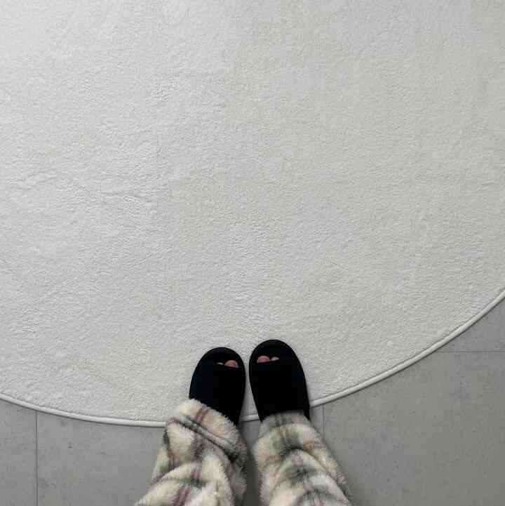 Soft white oval rug with black indoor slippers seen from above, creating a cozy atmosphere