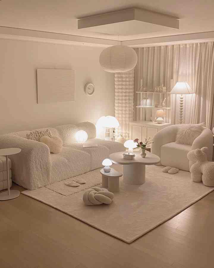 柔らかなホワイトトーンのリビング、曲線のソファとアームチェア、複数の照明が配置された雰囲気のあるインテリア