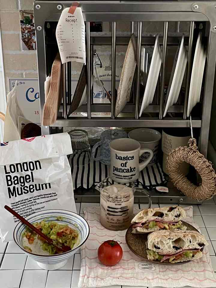 Beige and ivory-toned kitchen space featuring a dish rack, pancake mug, and a cozy brunch table with sandwich and guacamole