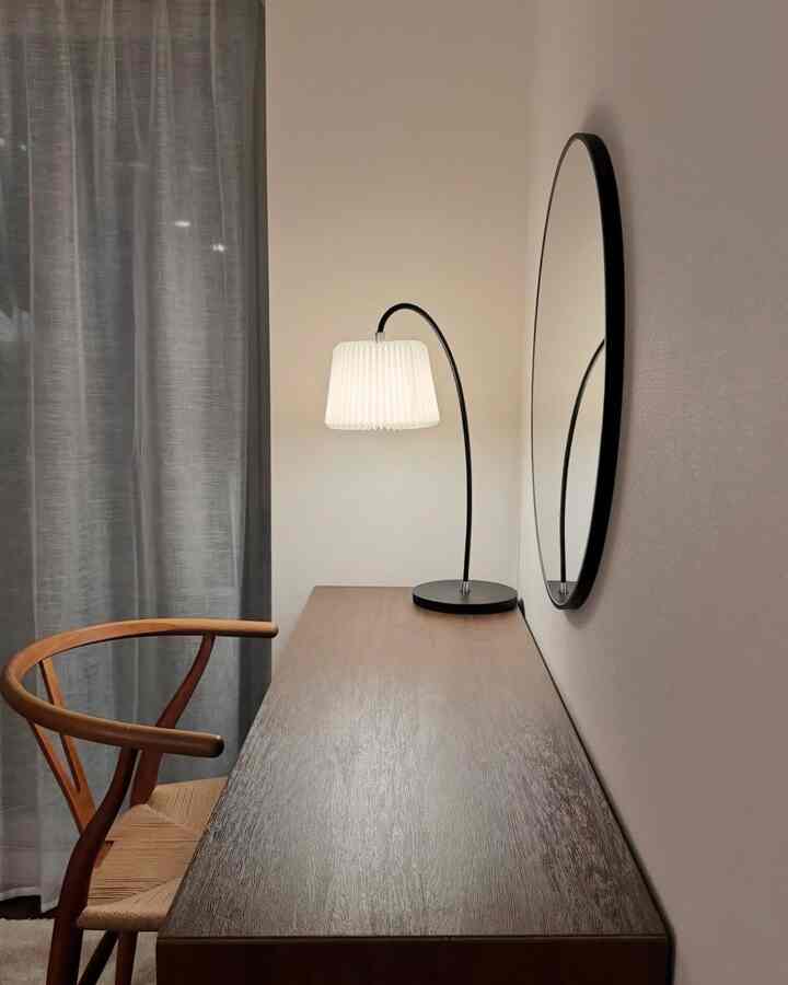 Natural toned home office space featuring wooden desk, vintage chair, Le Klint Snowdrop table lamp, and round wall mirror with simple design