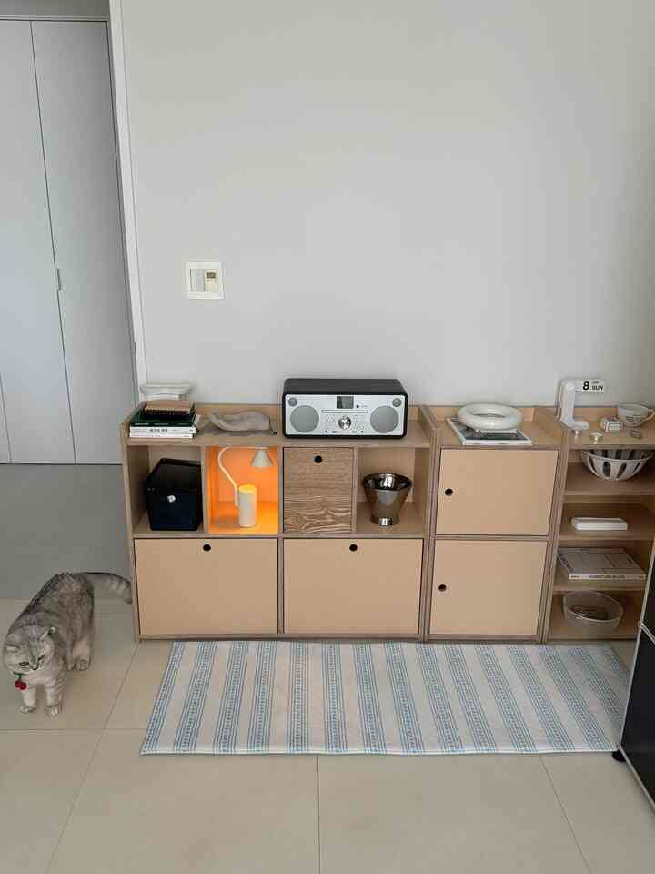 白とベージュの色調のリビングルーム、棚とキャビネットが配置された清潔感のある落ち着いた空間