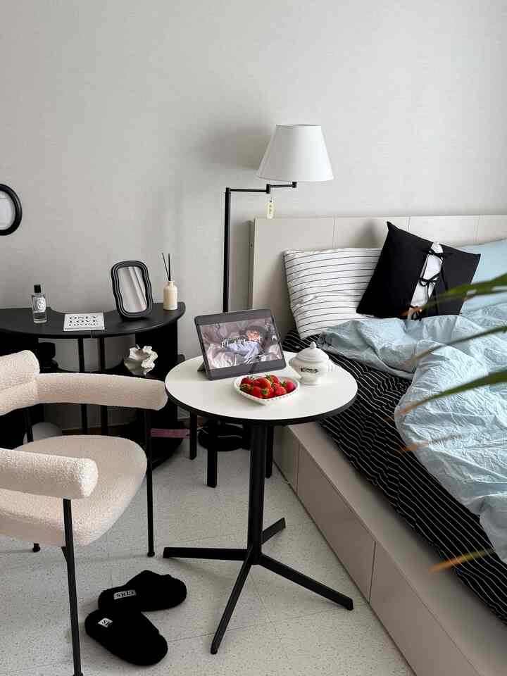 白と黒のトーンの寝室、サイドテーブルとアームチェアが配置された清潔感のある空間