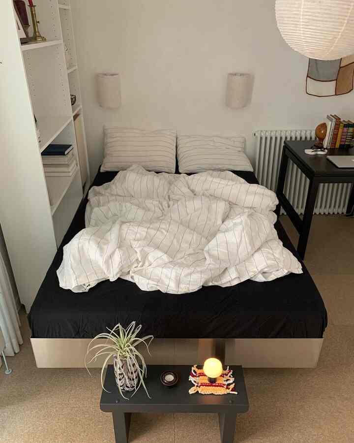 ナチュラルなベージュトーンの寝室、黒いマットレスとストライプのリネン寝具が配置されたミニマルな空間