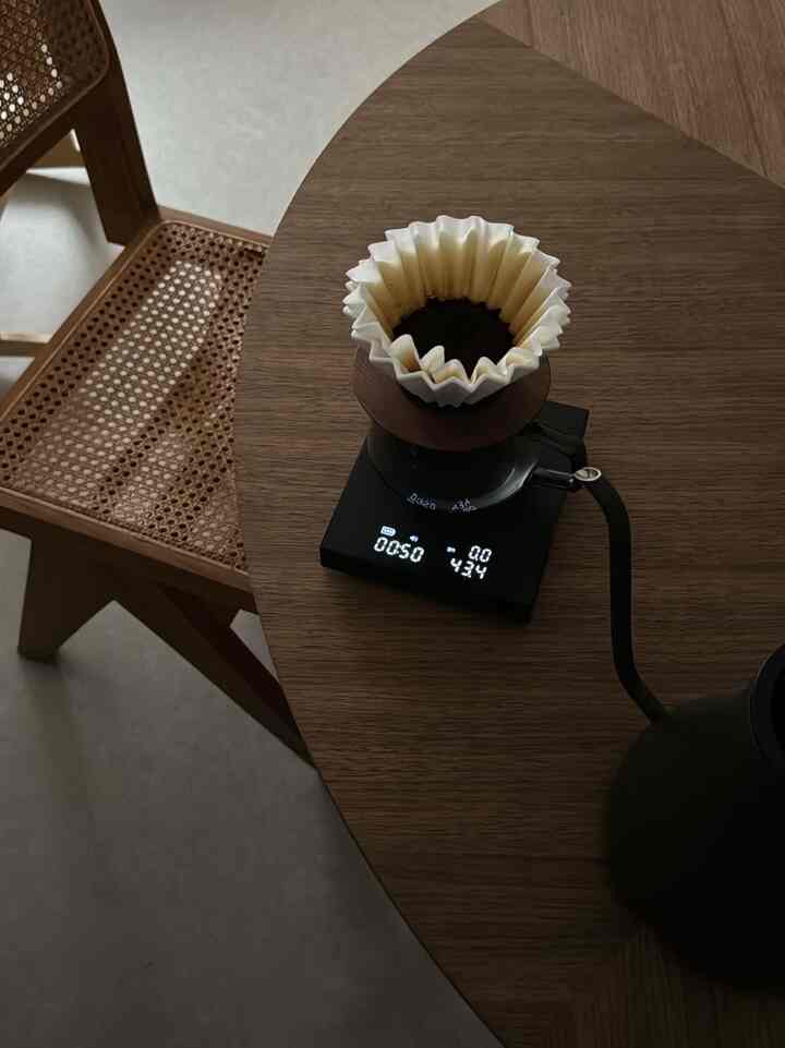 ナチュラルな木目調テーブルにハンドドリップコーヒーセットと黒い電気ケトルが配置されたアパートのホームカフェ空間