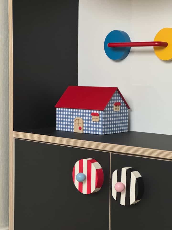 黒と白の収納キャビネットの上に赤い屋根のチェック柄の装飾用の家が置かれたシンプルなインテリア