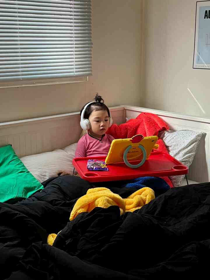 白い壁とブラインドのある寝室で、大きな赤いトレイの上でタブレットを見る赤ちゃんが配置された、雰囲気のある空間