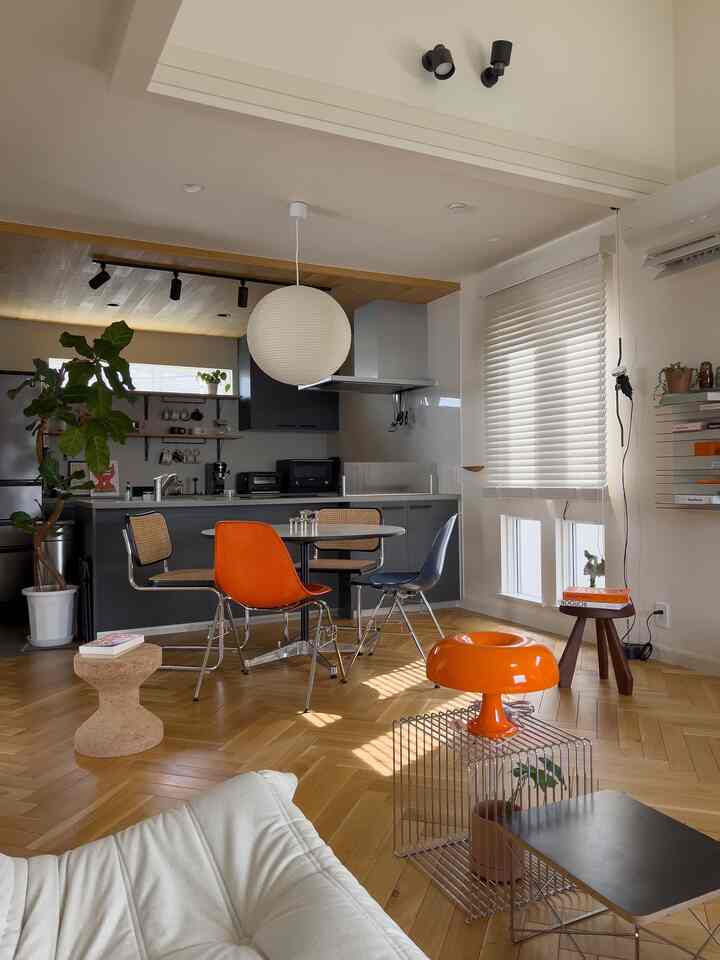 ナチュラルな木目調の床とオレンジ色のアクセントチェアがあるモダンなダイニングルームとキッチンスペース