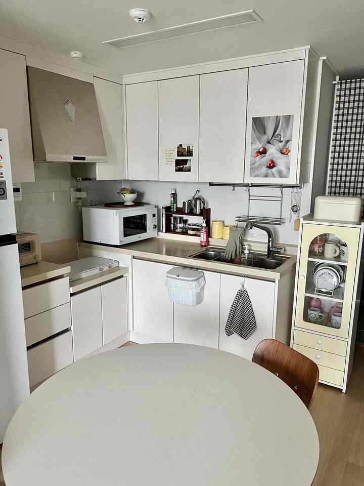 ホワイトとベージュのトーンのコンパクトなキッチン、丸いダイニングテーブルと整理されたキャビネットが配置された落ち着いた雰囲気の空間