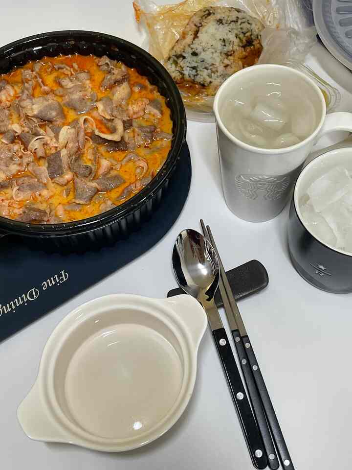 モノトーンの食卓に韓国風のマラータンとご飯、シルバーのカトラリーセットが配置されたフードデリバリーの食事風景