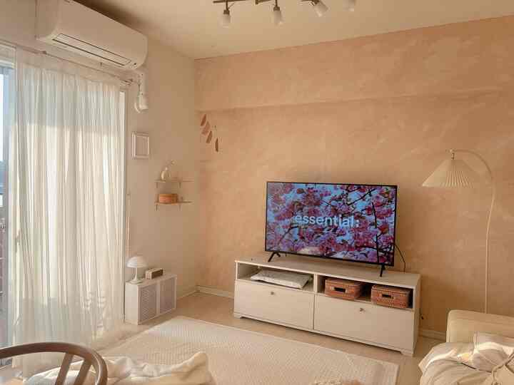 ベージュとアイボリーの色調のリビング、テレビとフロアランプが配置されたナチュラルでミニマルなインテリア