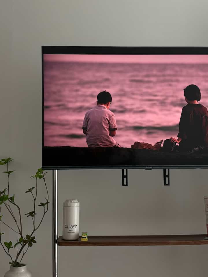 白い壁のナロールームリビング、レトロウッドの移動式テレビ台と植物が配置された自然な雰囲気のあるインテリア